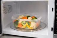 Boîte en plastique compatible placée dans un micro-ondes avec des légumes
