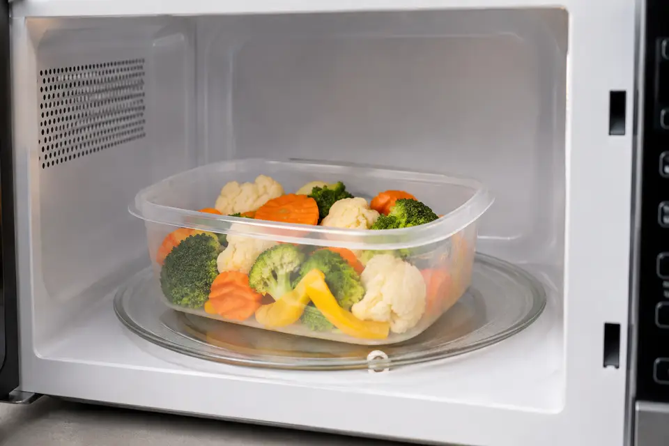 Boîte en plastique compatible placée dans un micro-ondes avec des légumes